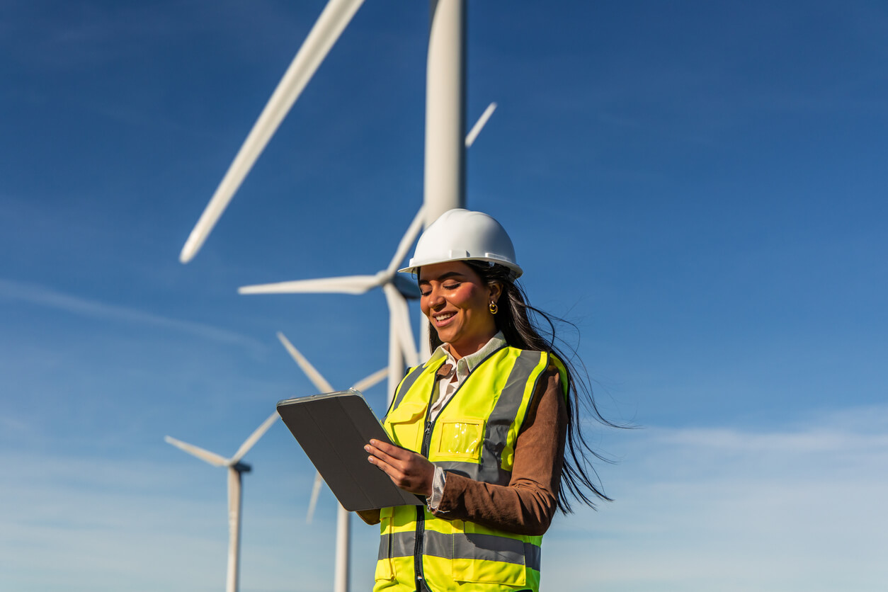 Female engineer inspecting wind turbines with digital tablet